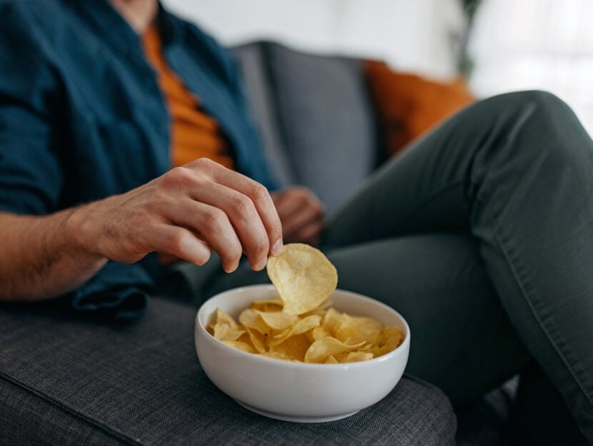 uomo che mangia patatine seduto sul divano