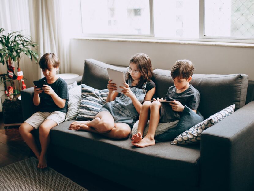 bambini sul divano che guardano il telefono e i tablet