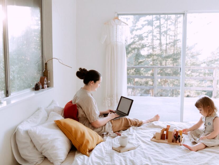 mamma e figlia sul letto mentre la mamma lavora al pc